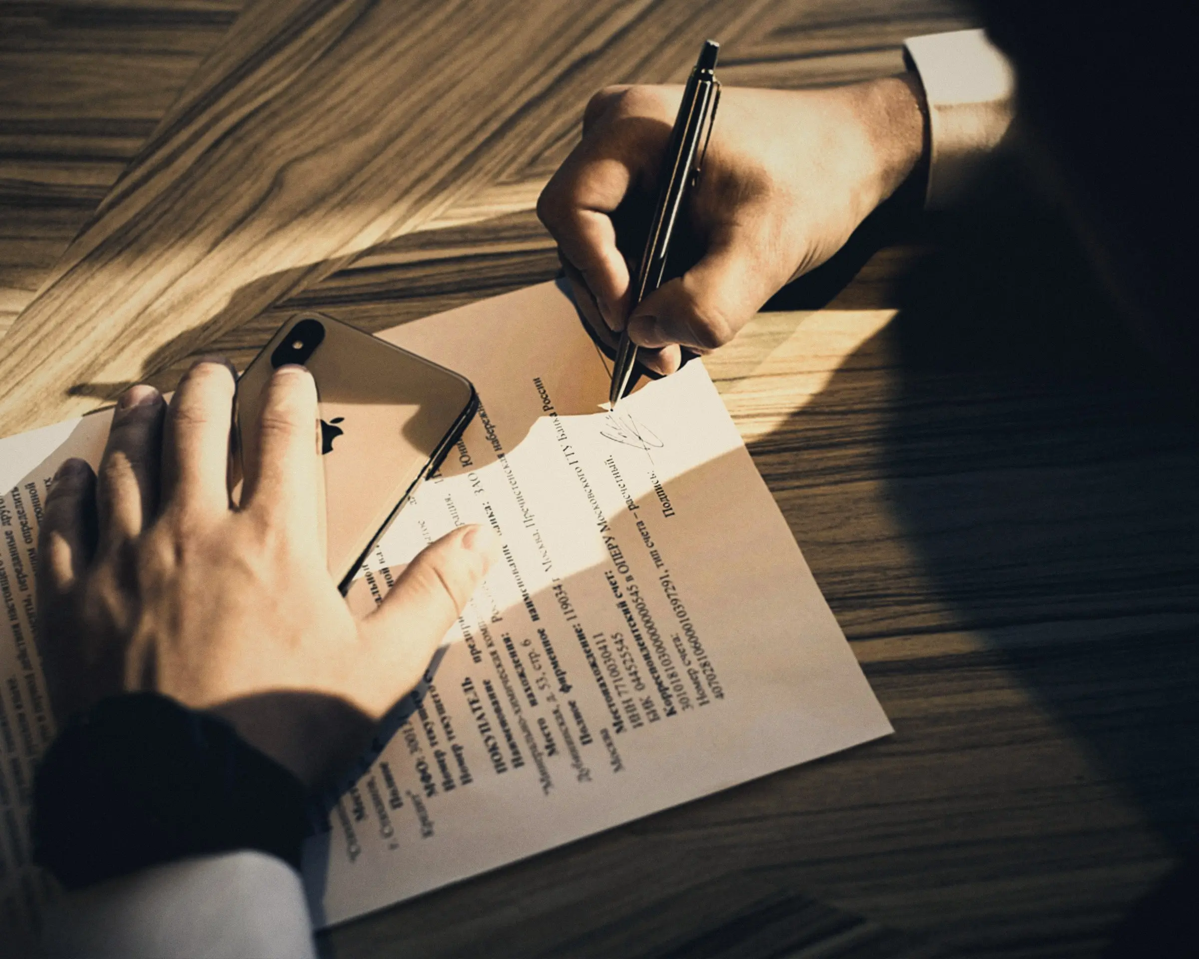 Mano firmando un contrato sobre una mesa de madera
