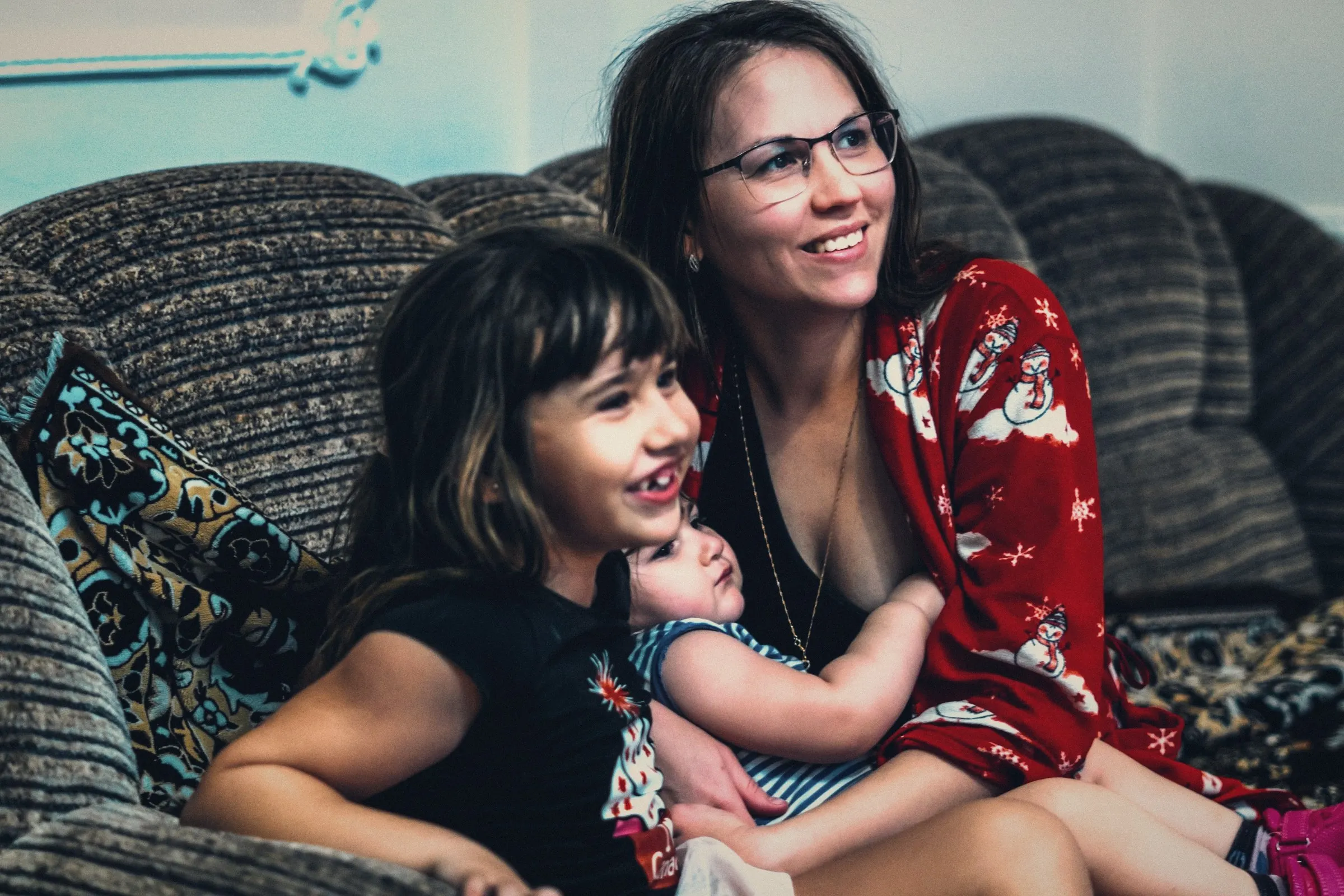 Mamá con sus hijas riendo en el sofá de su casa