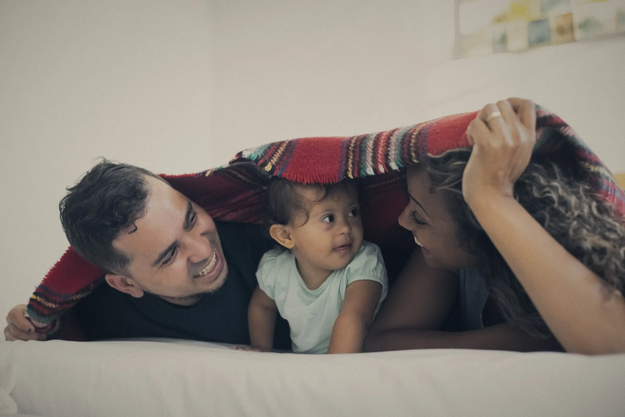 Familia riendo y jugando bajo una cobija en casa