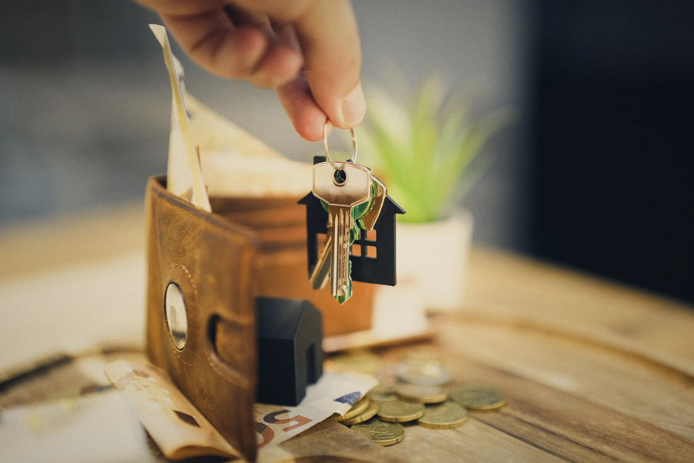 Mano que sostiene las llaves de una vivienda sobre una billetera con dinero